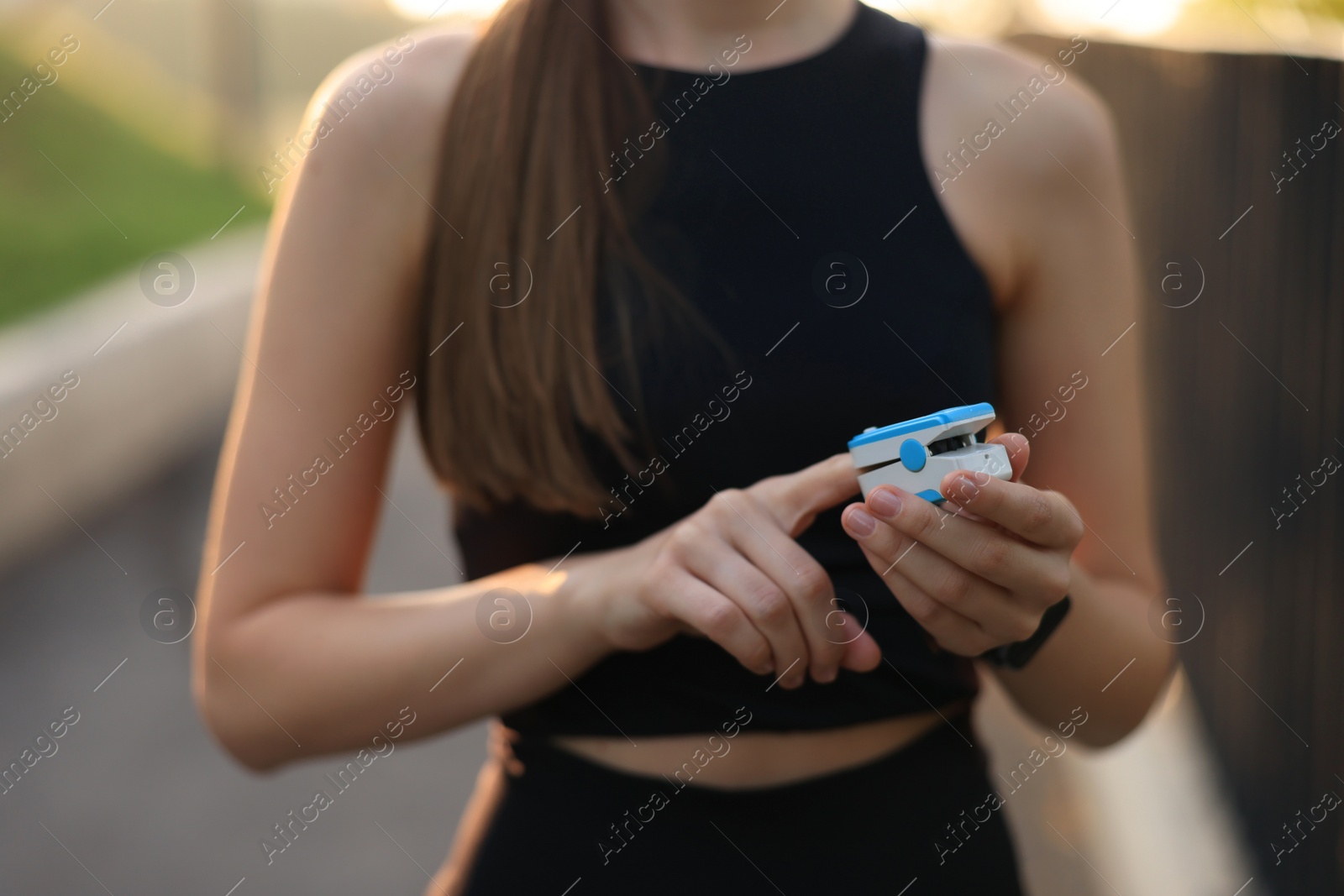 Photo of Woman checking pulse with blood pressure monitor on finger after training outdoors, closeup