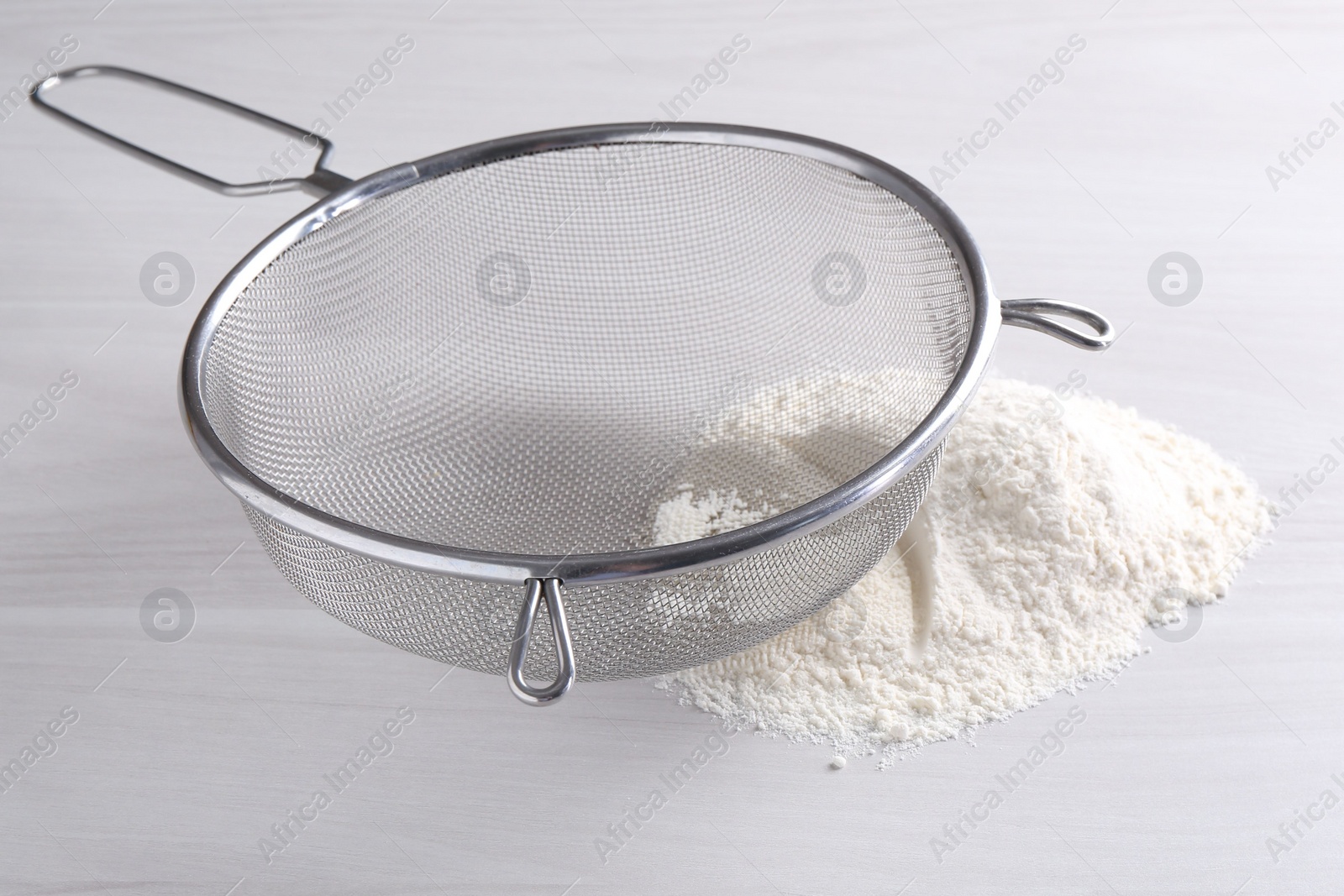 Photo of Metal sieve and flour on white wooden table