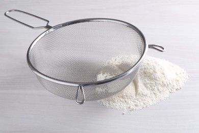 Metal sieve and flour on white wooden table