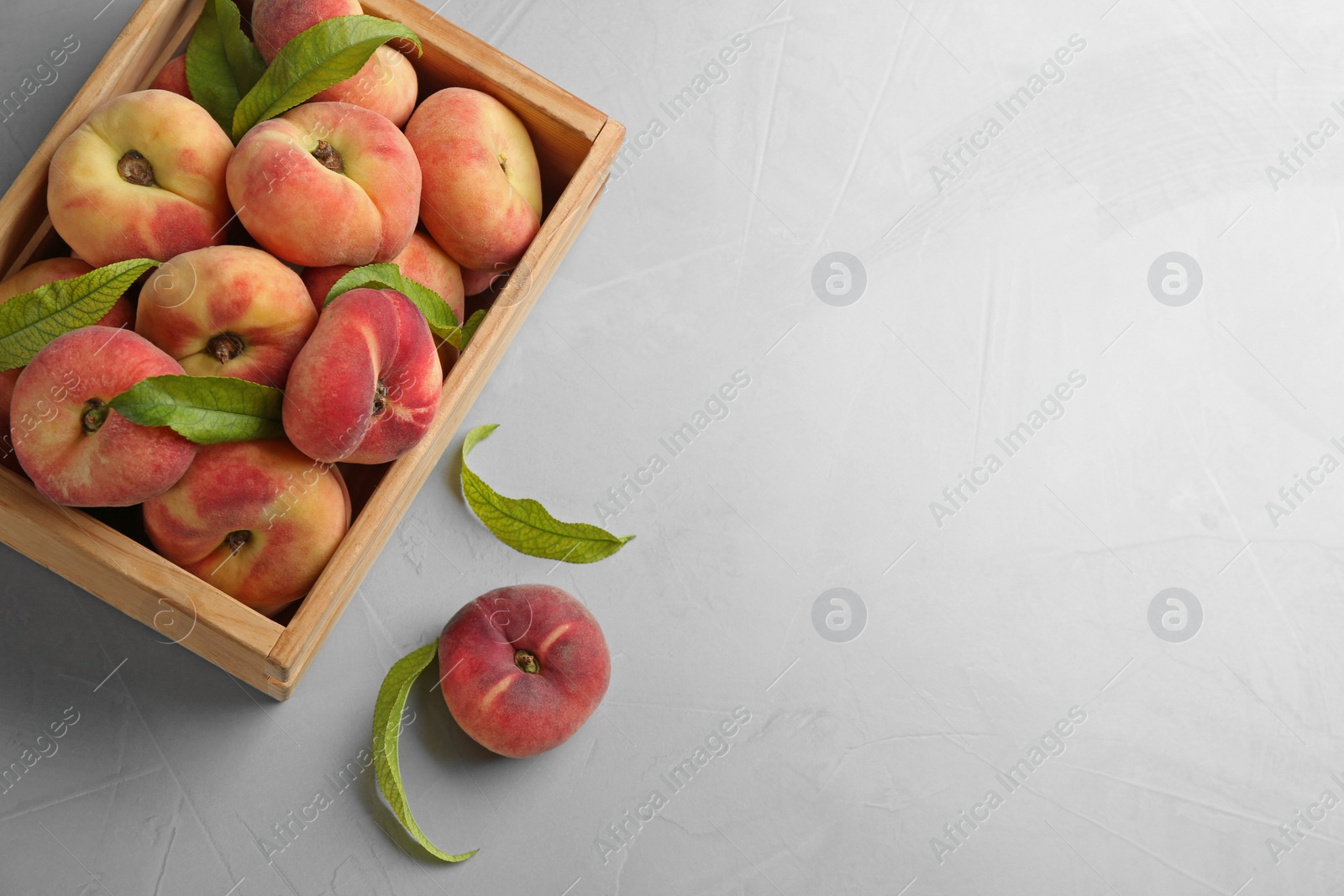 Photo of Fresh ripe donut peaches with leaves on light table, flat lay. Space for text