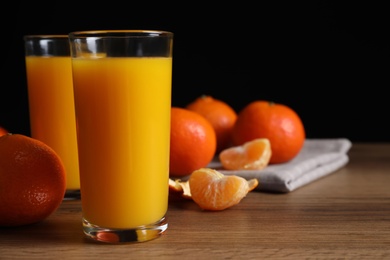 Glasses of fresh tangerine juice and fruits on wooden table, space for text
