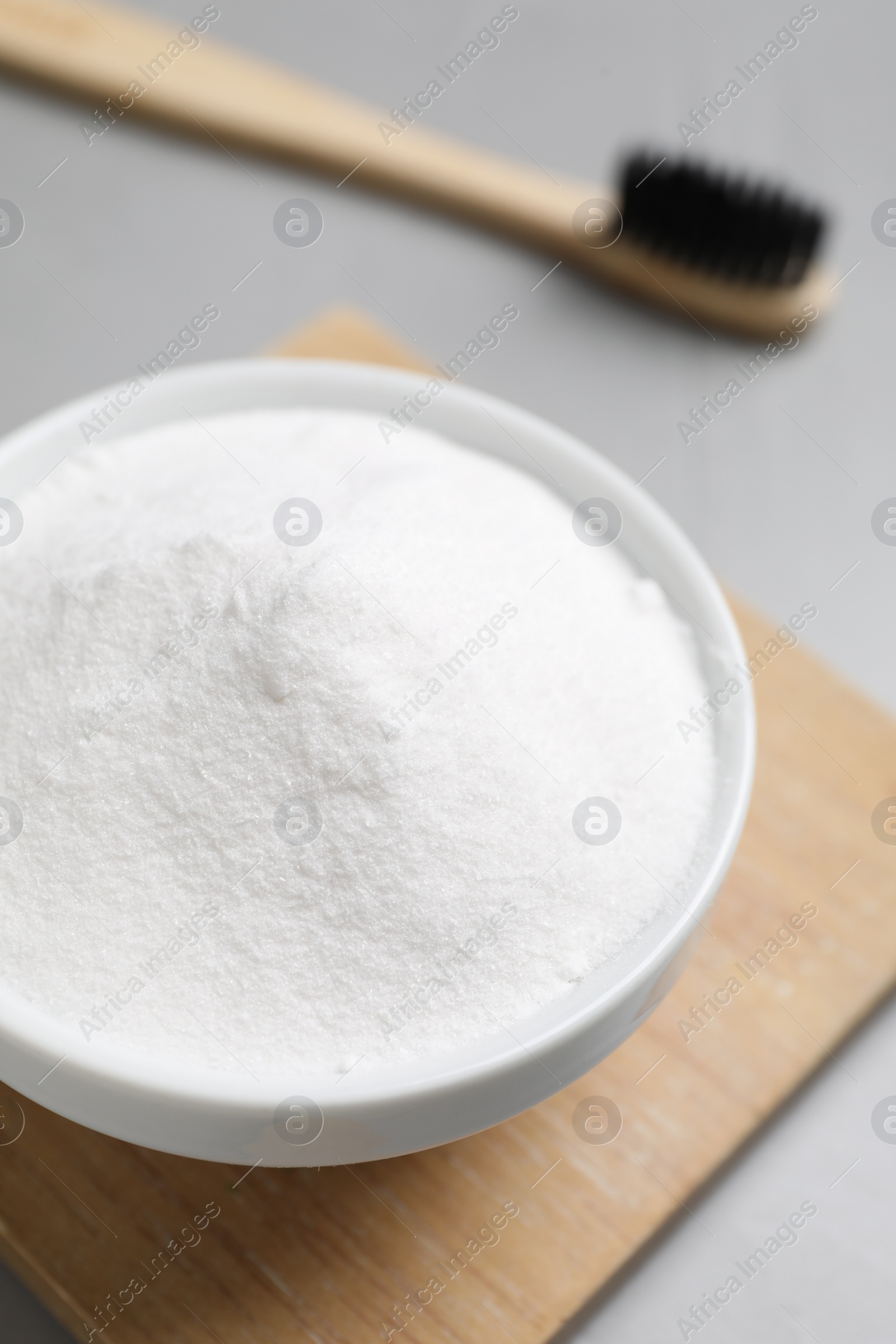 Photo of Bamboo toothbrush and bowl of baking soda on grey table, closeup