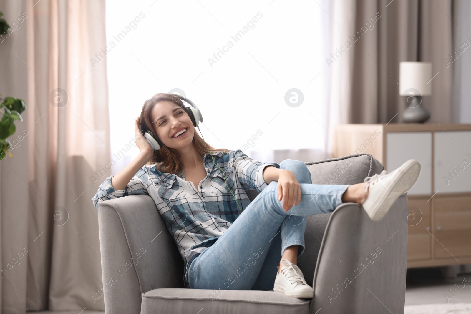 Photo of Young woman with headphones resting in armchair at home