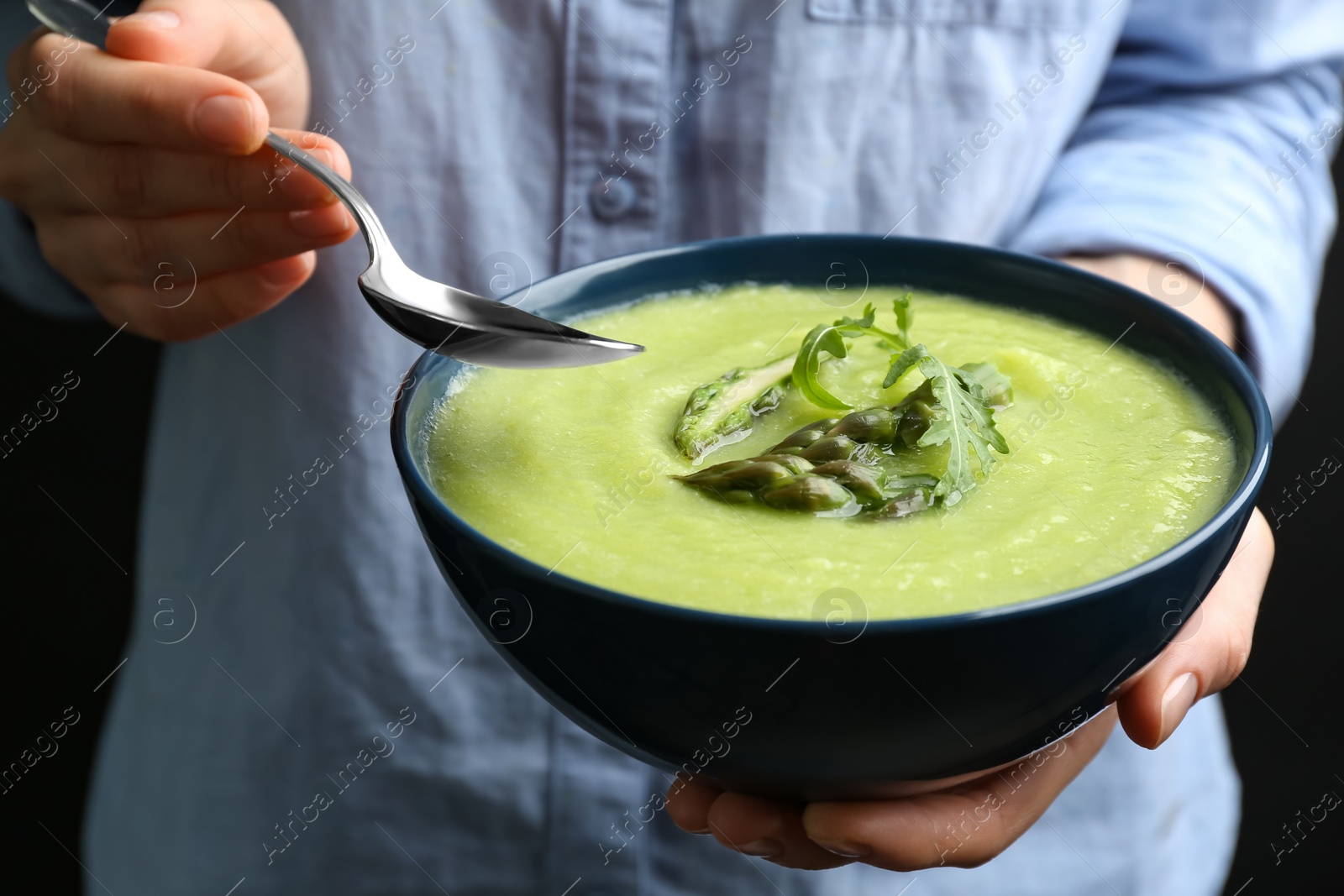 Photo of Woman eating delicious asparagus soup on black background, closeup