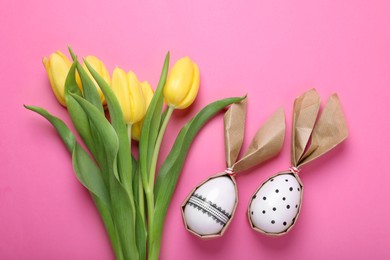 Photo of Easter bunnies made of craft paper and eggs near beautiful tulips on pink background, flat lay