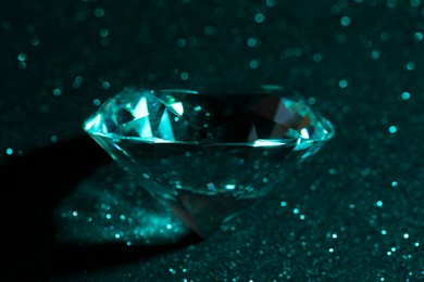 Photo of Beautiful dazzling diamond on green glitter surface, closeup