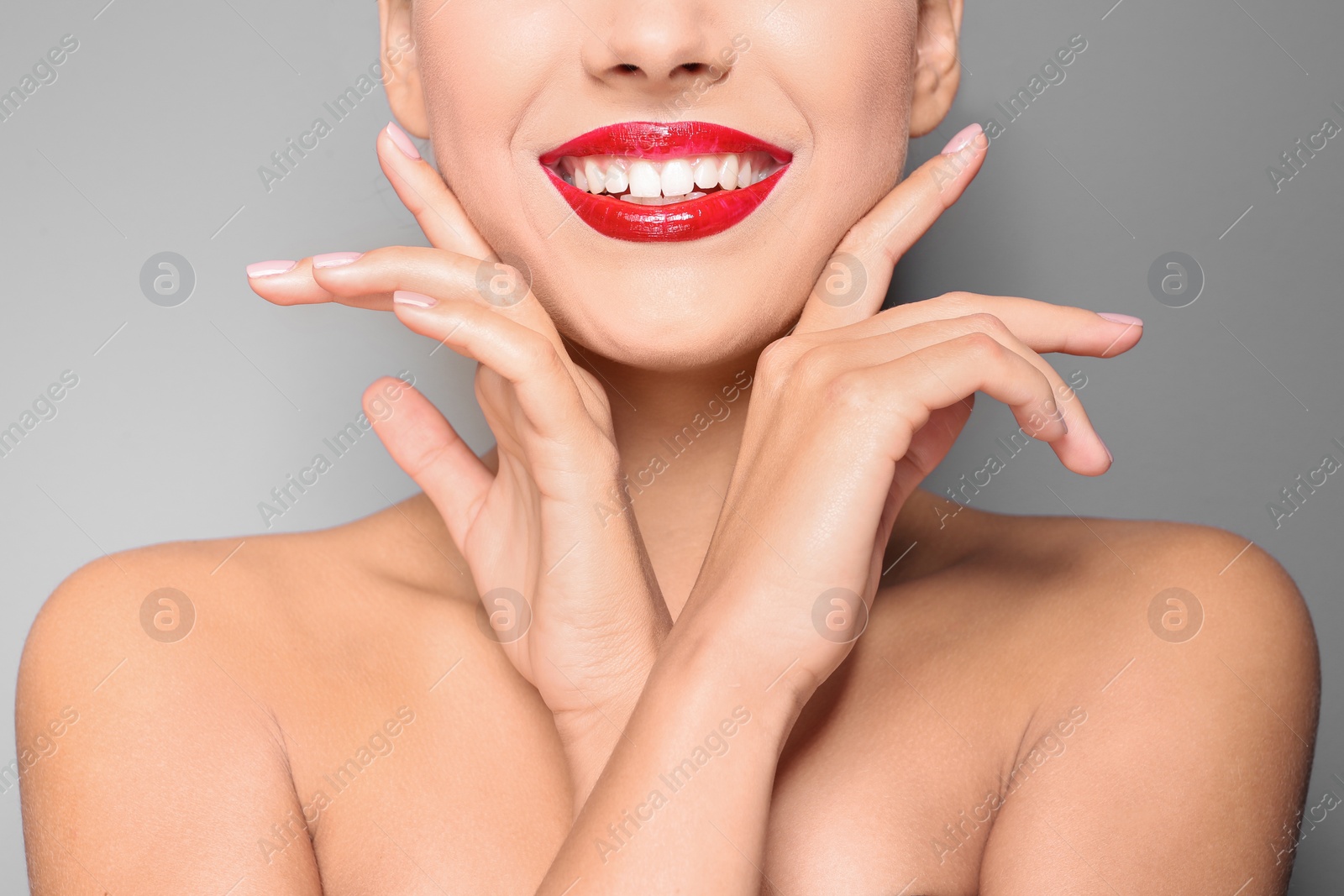 Photo of Beautiful young woman with red glossy lips on gray background, closeup