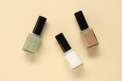 Photo of Colorful nail polishes in bottles on beige background, flat lay