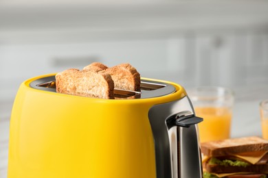 Photo of Modern yellow toaster with roasted bread slices on table, closeup