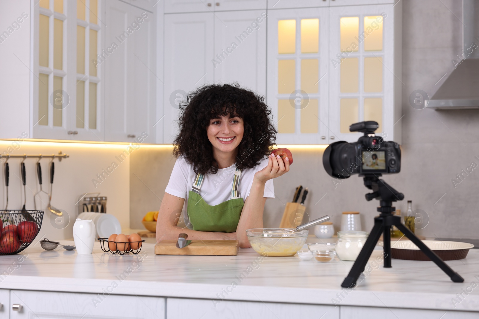 Photo of Smiling food blogger explaining something while recording video in kitchen