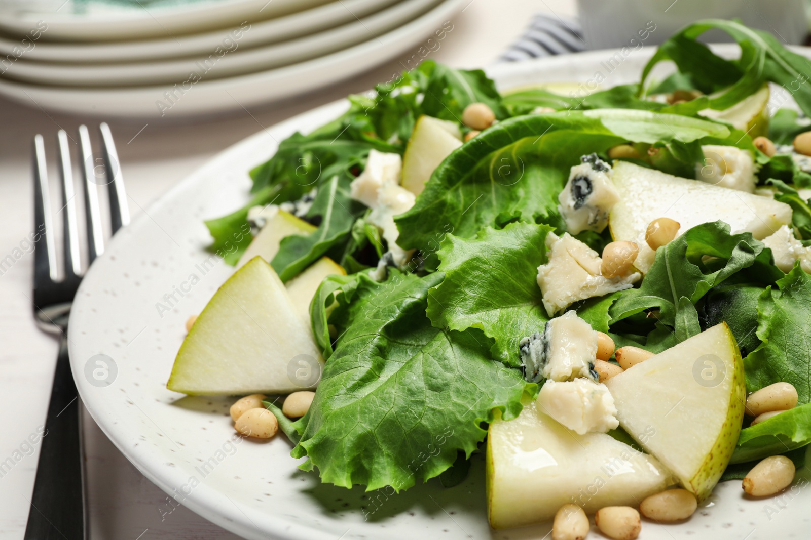 Photo of Tasty salad with pear slices, lettuce and pine nuts in plate, closeup