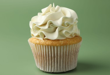 Tasty vanilla cupcake with cream on green background, closeup