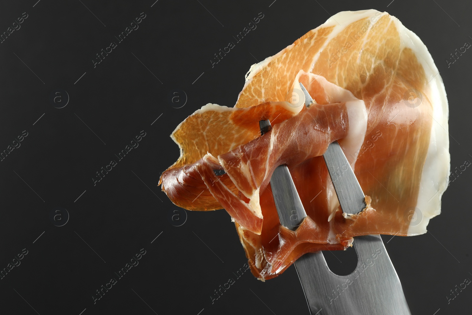 Photo of Fork with slice of tasty jamon on black background, closeup. Space for text