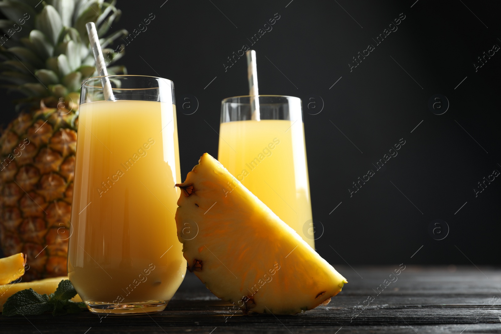 Photo of Delicious pineapple juice and fresh fruit on black wooden table, closeup