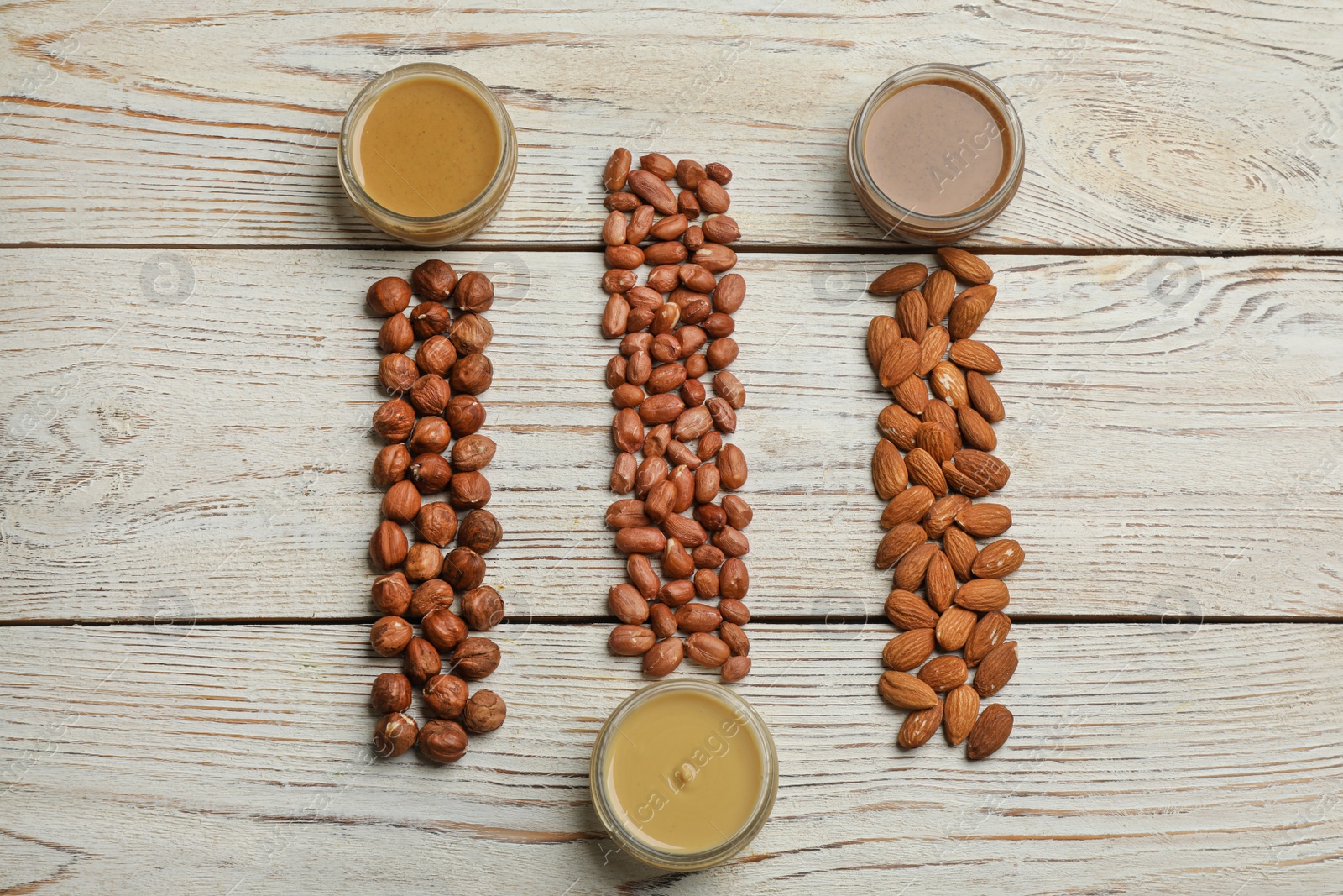 Photo of Jars with butters made of different nuts and ingredients on white wooden table, flat lay