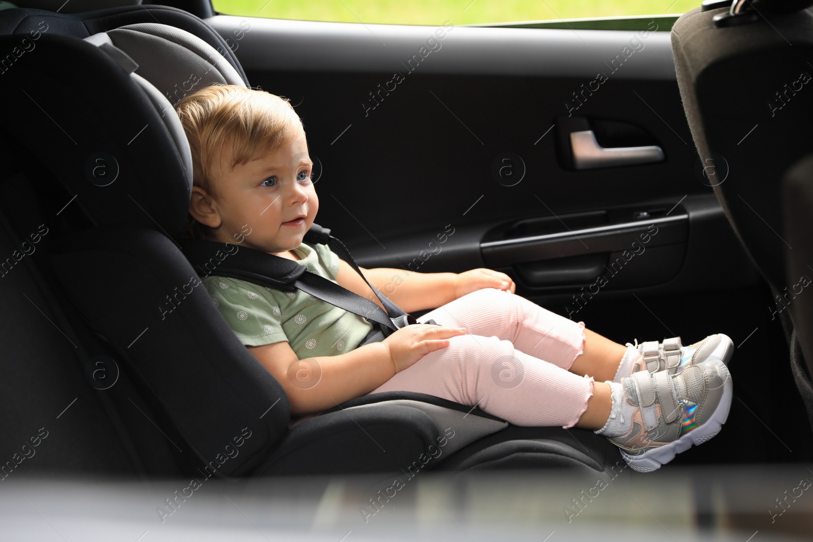 Photo of Cute little girl sitting in child safety seat inside car