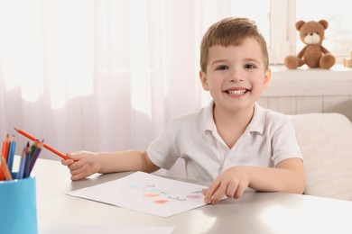 Photo of Cute little boy drawing with pencil at light table in room. Child`s art