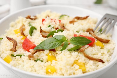 Photo of Bowl of delicious couscous with vegetables and basil, closeup