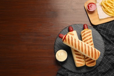 Photo of Delicious french hot dogs, fries and dip sauces on wooden table, flat lay. Space for text