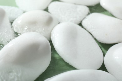 Spa stones in water on light green background, closeup