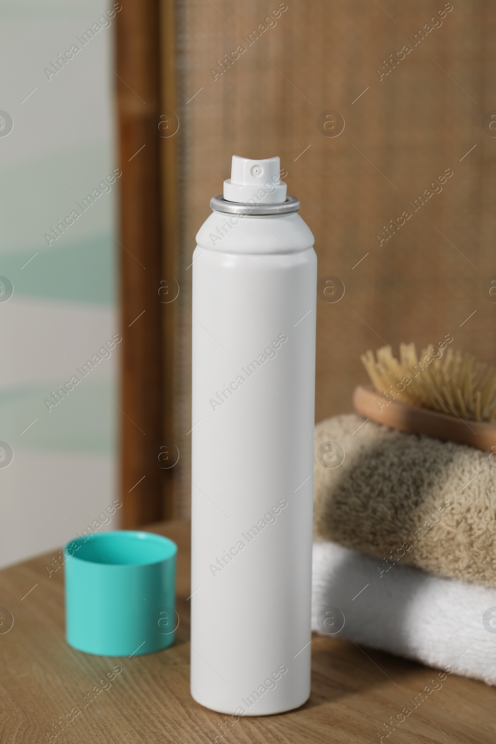 Photo of Bottle of dry shampoo, towels and hairbrush on wooden table indoors