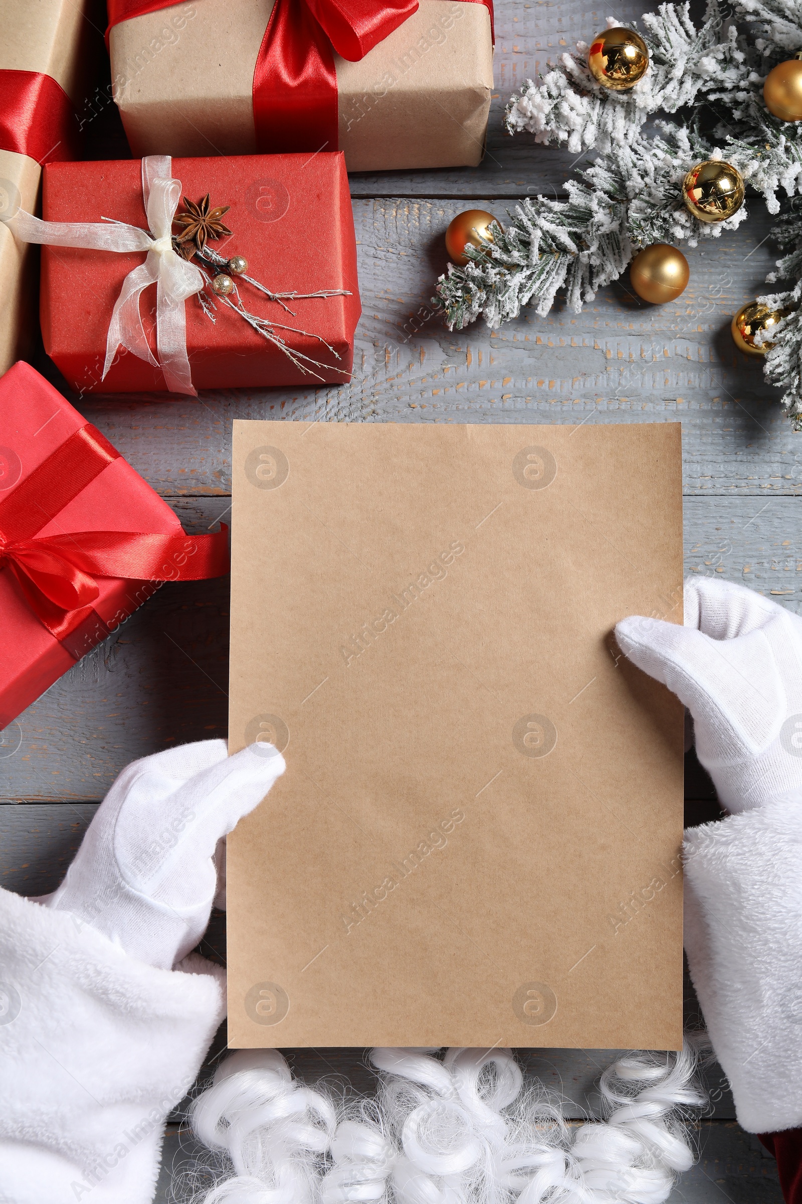 Photo of Santa Claus with letter, gift boxes and Christmas decor at grey wooden table, top view. Space for text