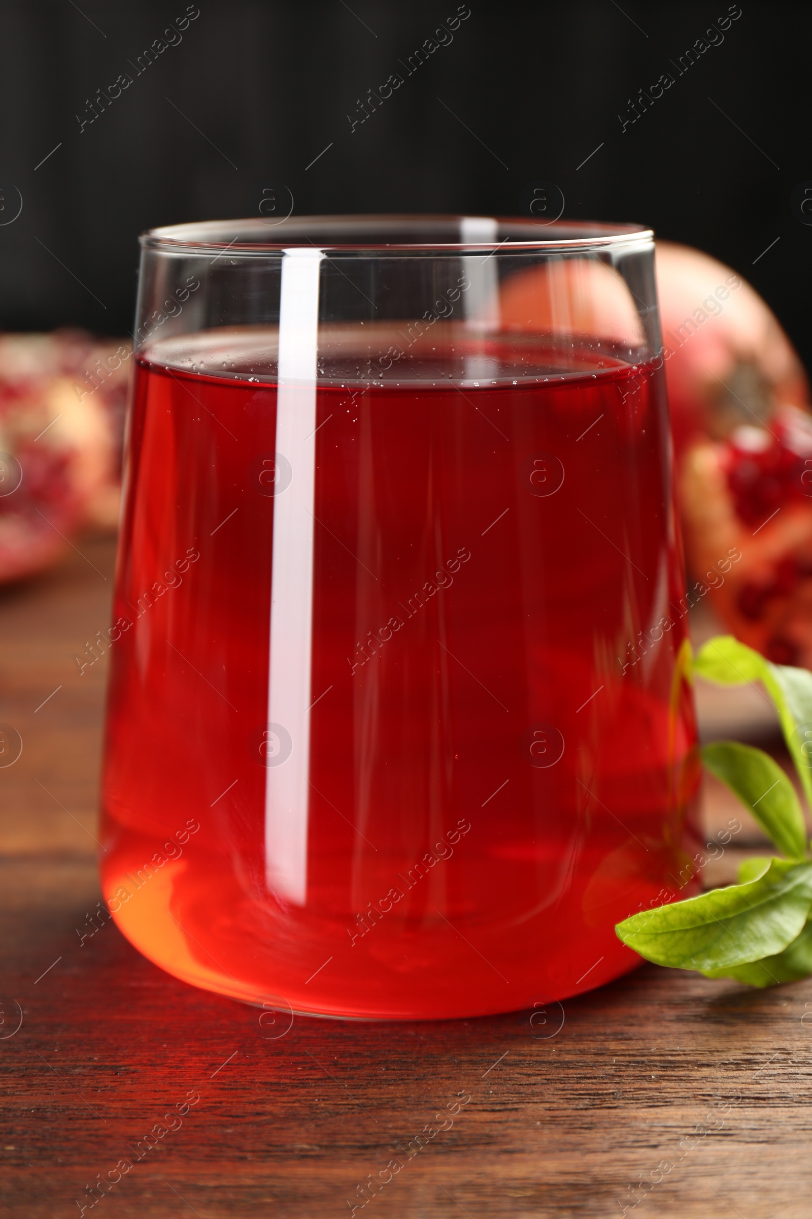 Photo of Tasty pomegranate juice in glass on wooden table, closeup