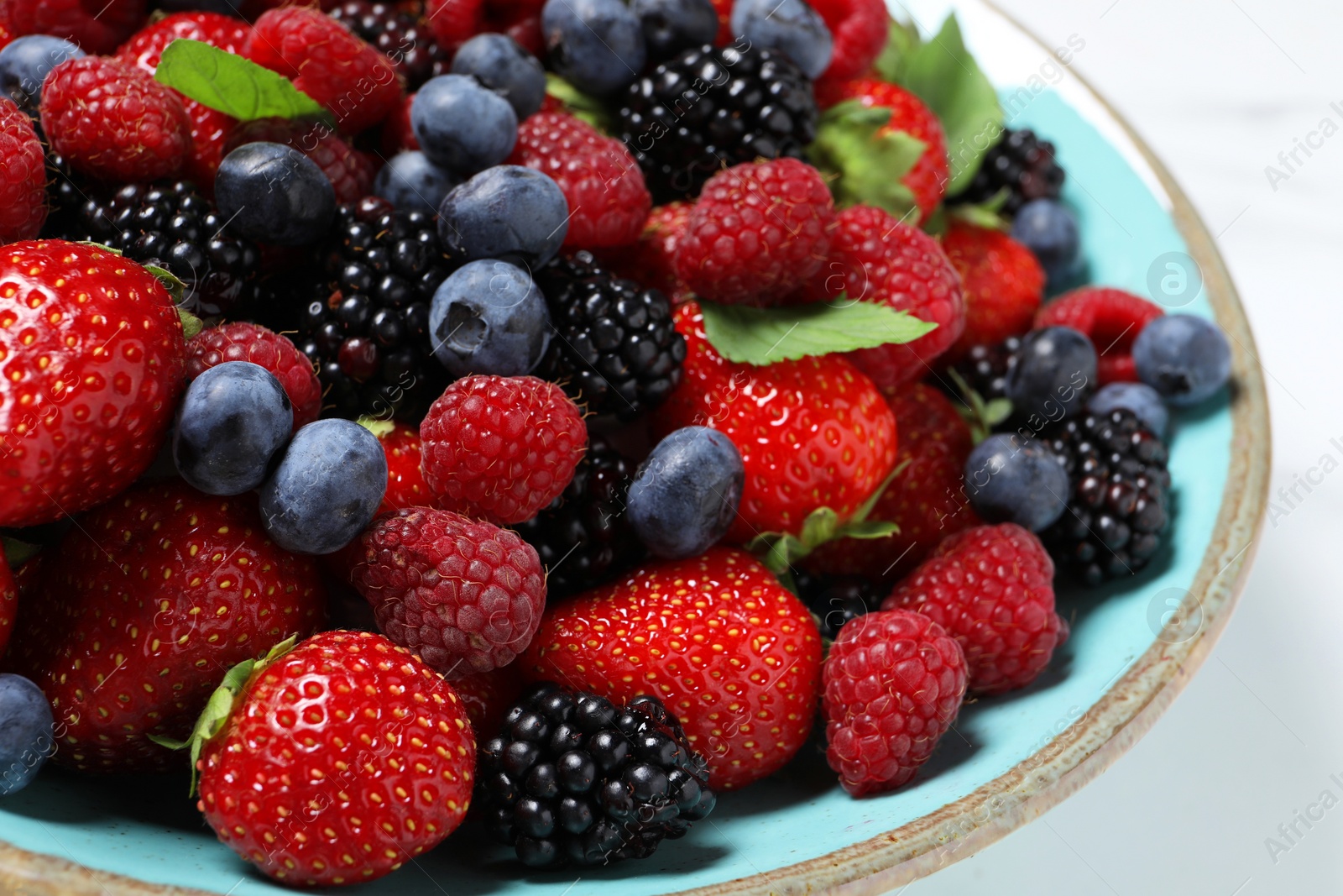 Photo of Many different fresh ripe berries in bowl on white table, closeup