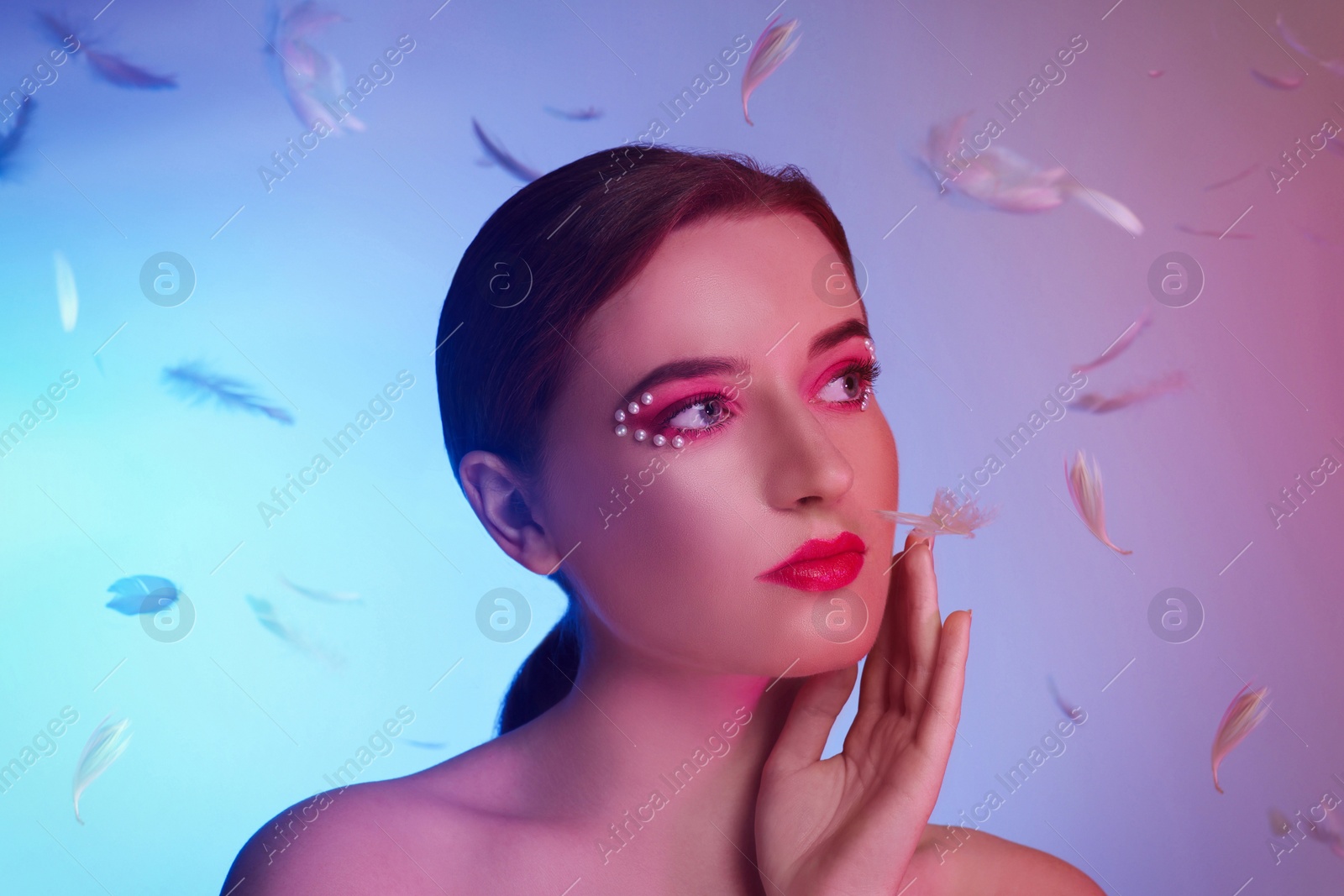 Photo of Fashionable portrait of beautiful young woman posing with falling feathers on colorful background