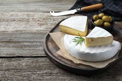 Photo of Tasty cut brie cheese with rosemary and olives on wooden table, space for text