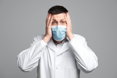 Portrait of doctor in protective mask feeling fear on grey background