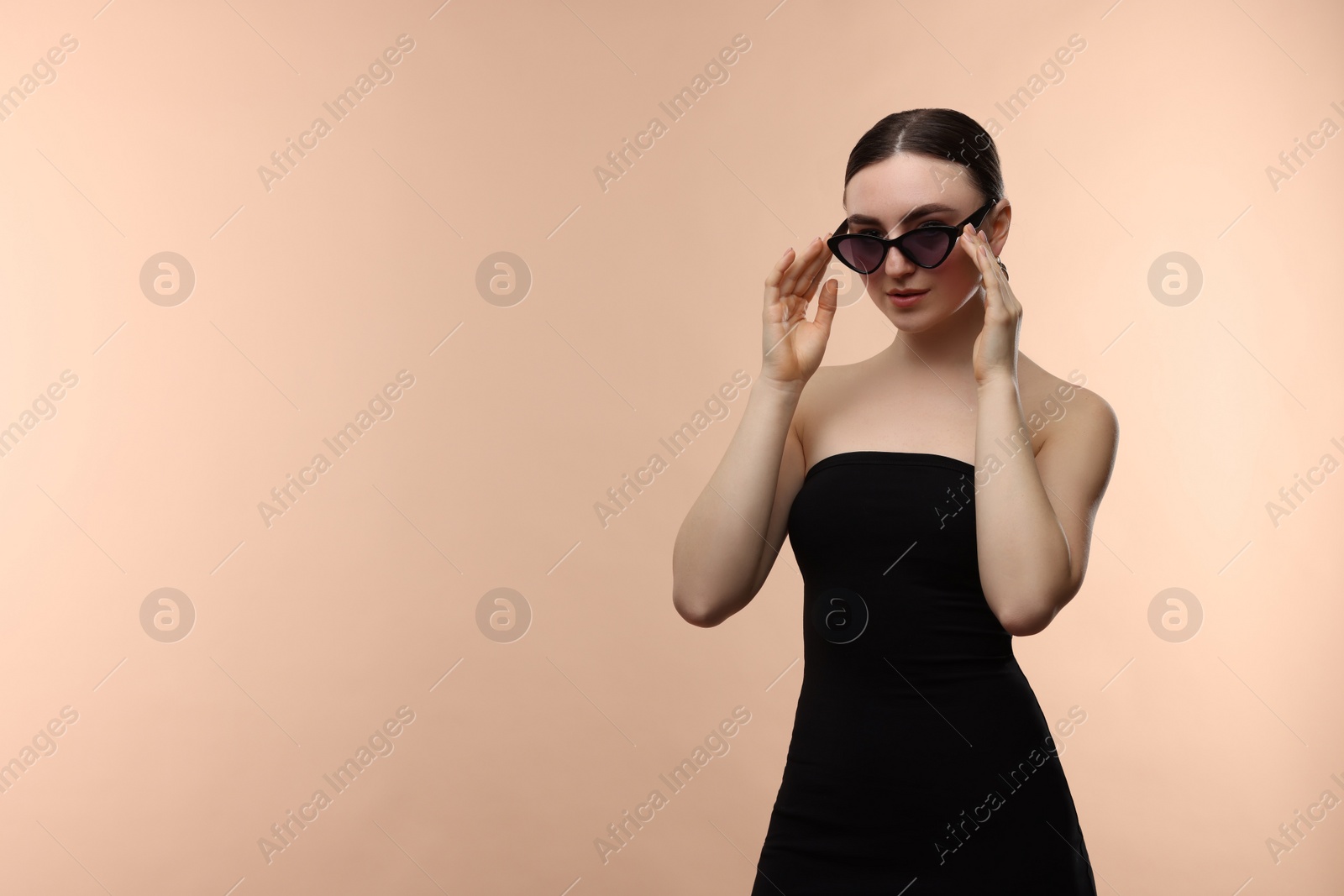 Photo of Portrait of beautiful young woman with sunglasses on beige background, space for text