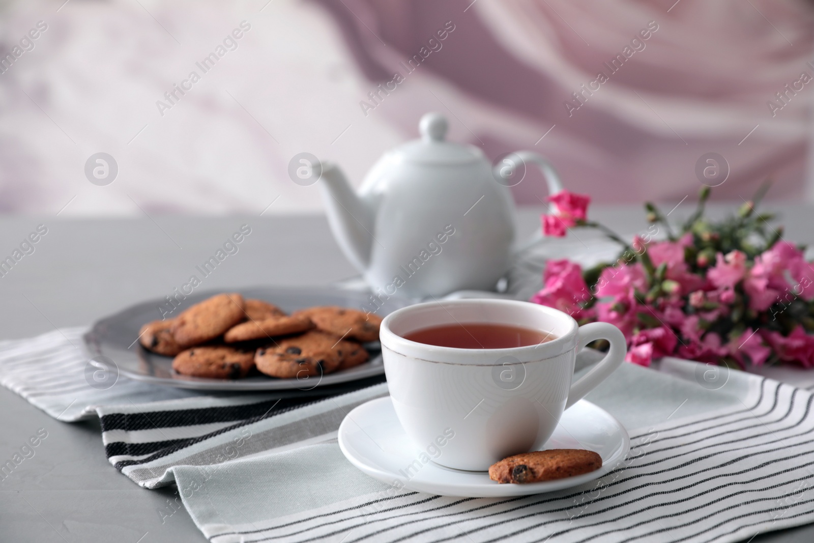 Photo of Cup of aromatic tea and tasty cookies on grey table