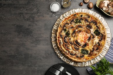 Photo of Delicious quiche with mushrooms and ingredients on dark grey table, flat lay. Space for text