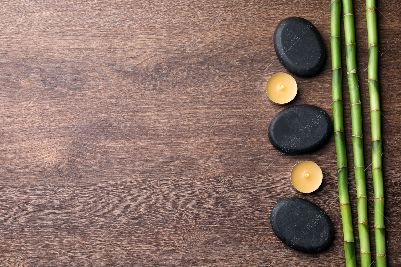 Photo of Spa stones, burning candles and bamboo stems on wooden table, flat lay. Space for text
