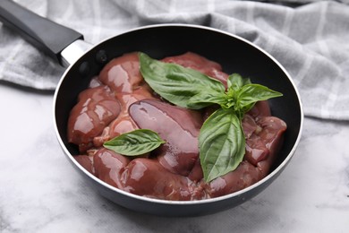 Photo of Raw chicken liver with basil in frying pan on white marble table, closeup