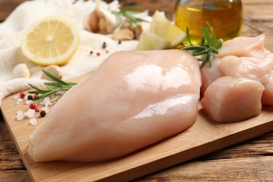 Photo of Fresh raw chicken breast with rosemary and spices on wooden table, closeup