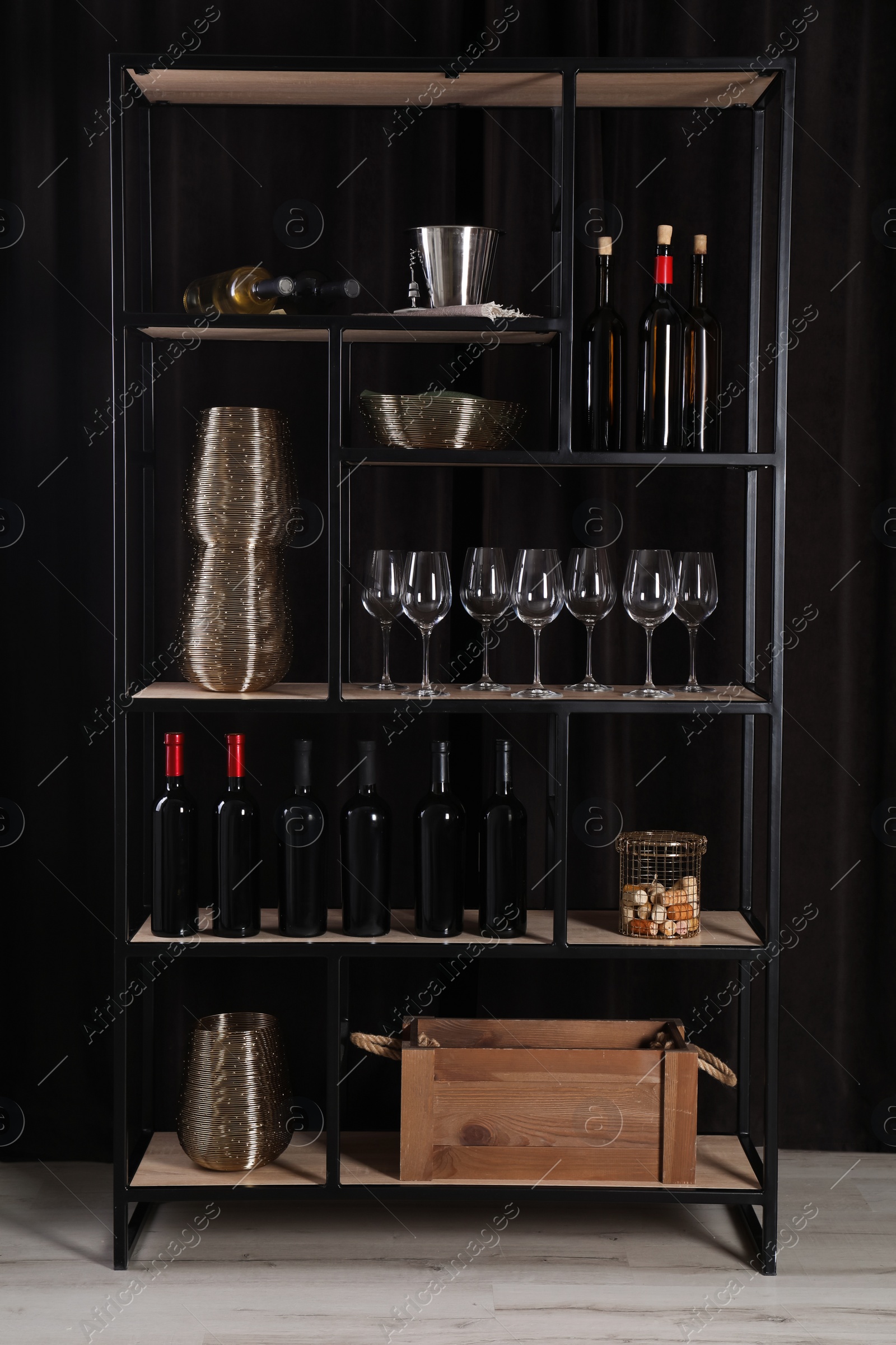 Photo of Rack with bottles of wine and glasses near black wall