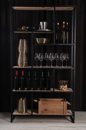 Photo of Rack with bottles of wine and glasses near black wall