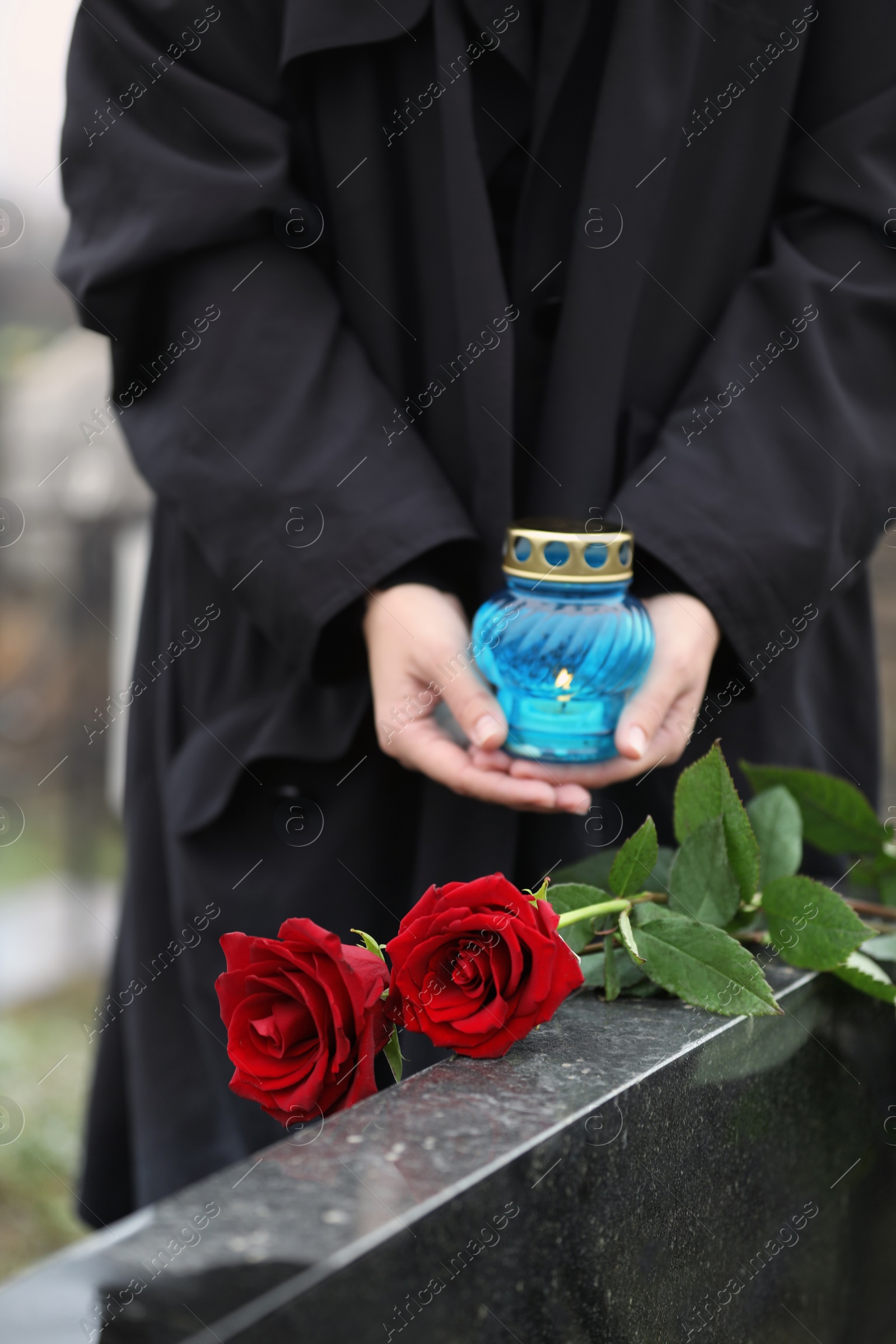 Photo of Woman with candle outdoors, focus on red roses. Funeral ceremony