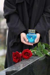 Woman with candle outdoors, focus on red roses. Funeral ceremony