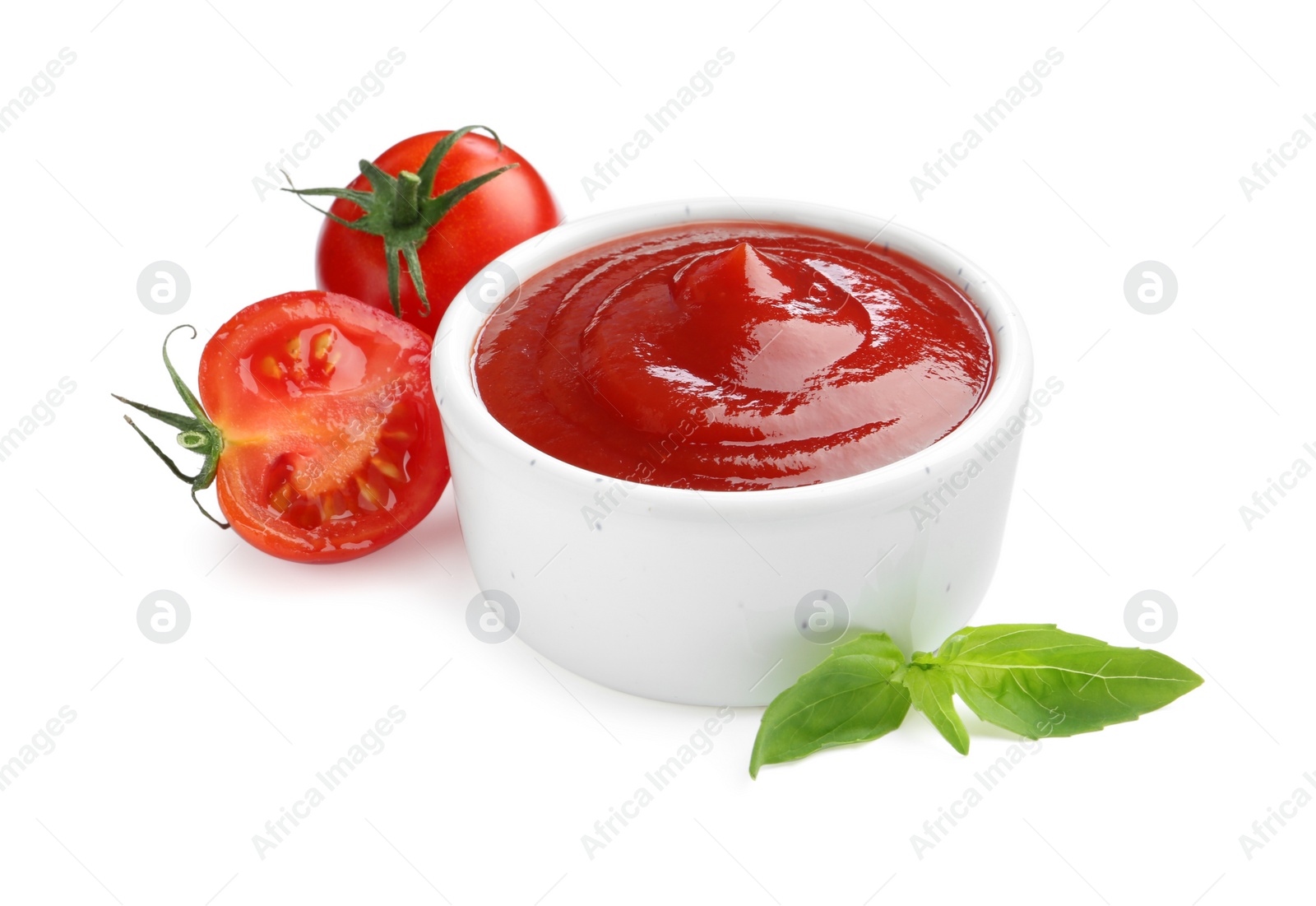 Photo of Tasty ketchup in bowl, basil and fresh tomatoes isolated on white