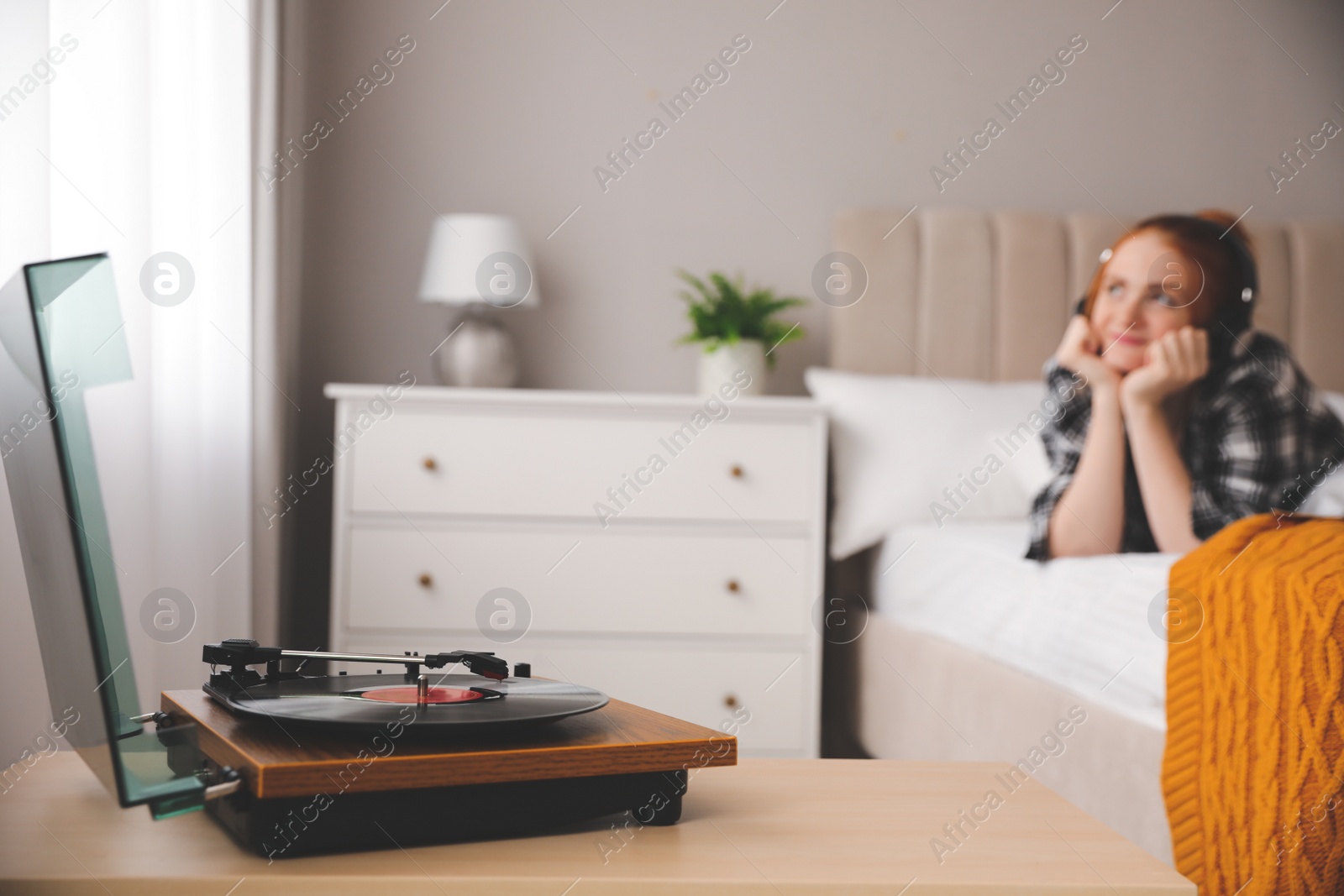 Photo of Young woman listening to music in bedroom, focus on turntable