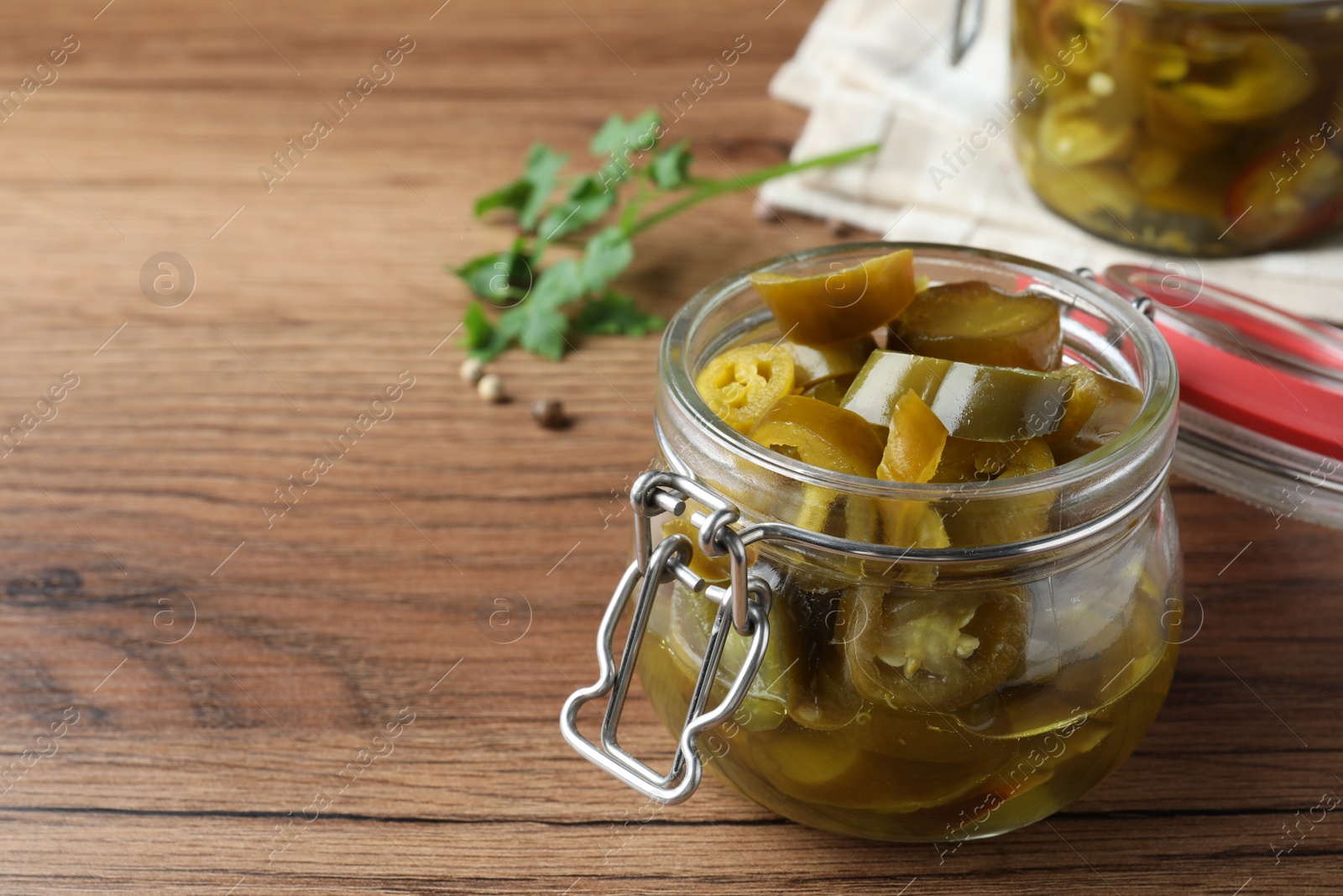 Photo of Glass jar with slices of pickled green jalapeno peppers on wooden table, space for text