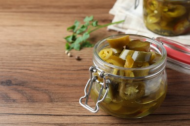 Photo of Glass jar with slices of pickled green jalapeno peppers on wooden table, space for text