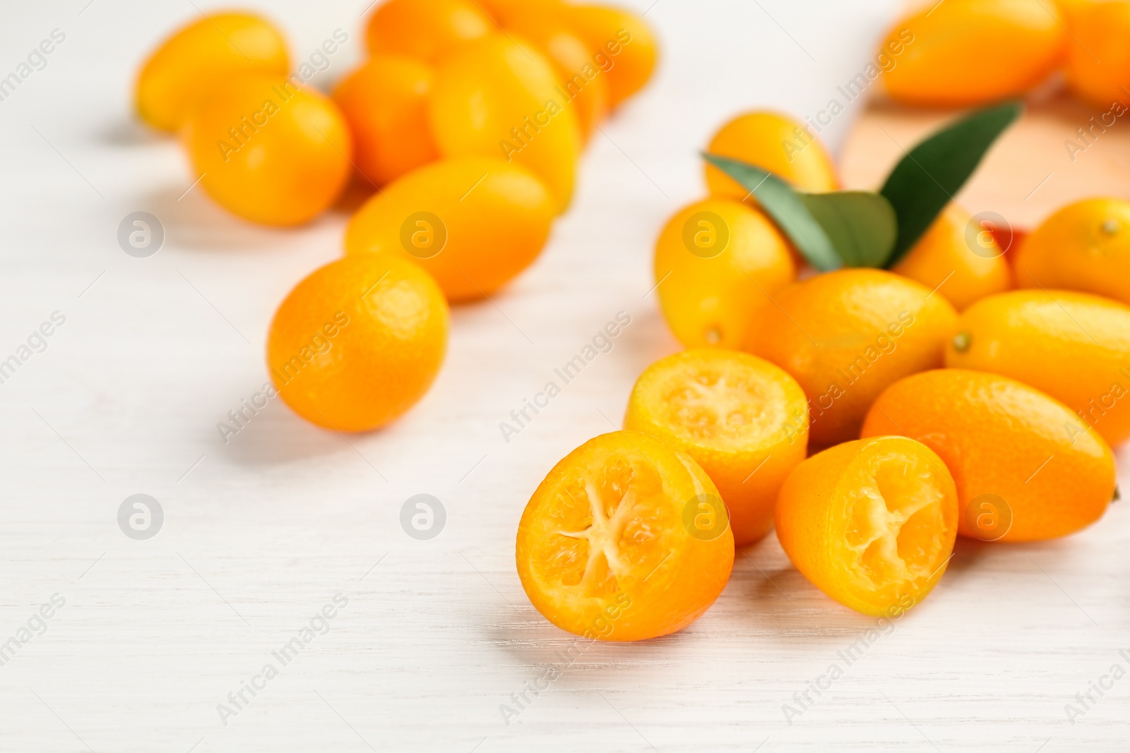 Photo of Fresh ripe kumquats with green leaves on white wooden table