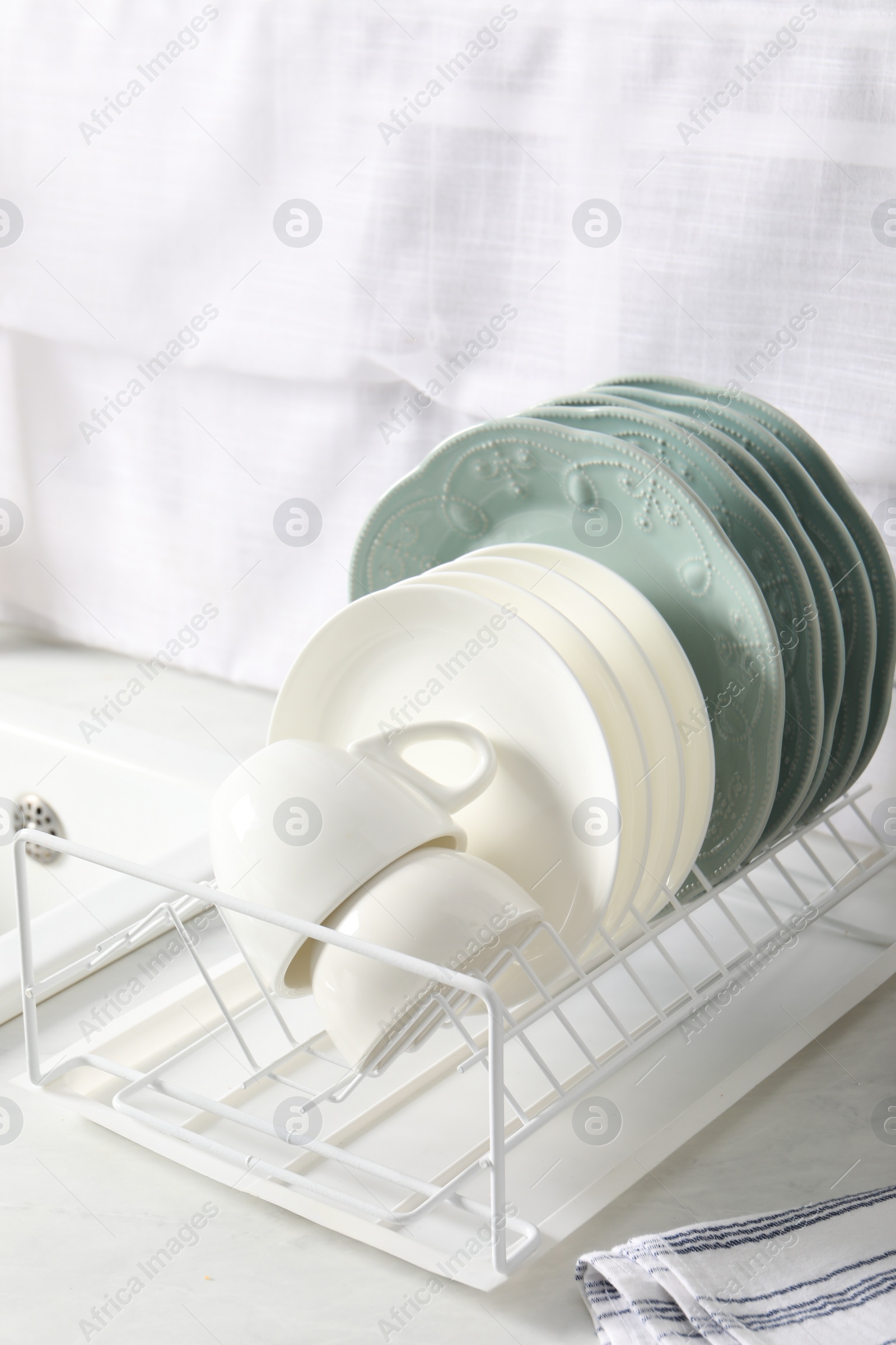 Photo of Drainer with different clean dishware and cups on white table in kitchen