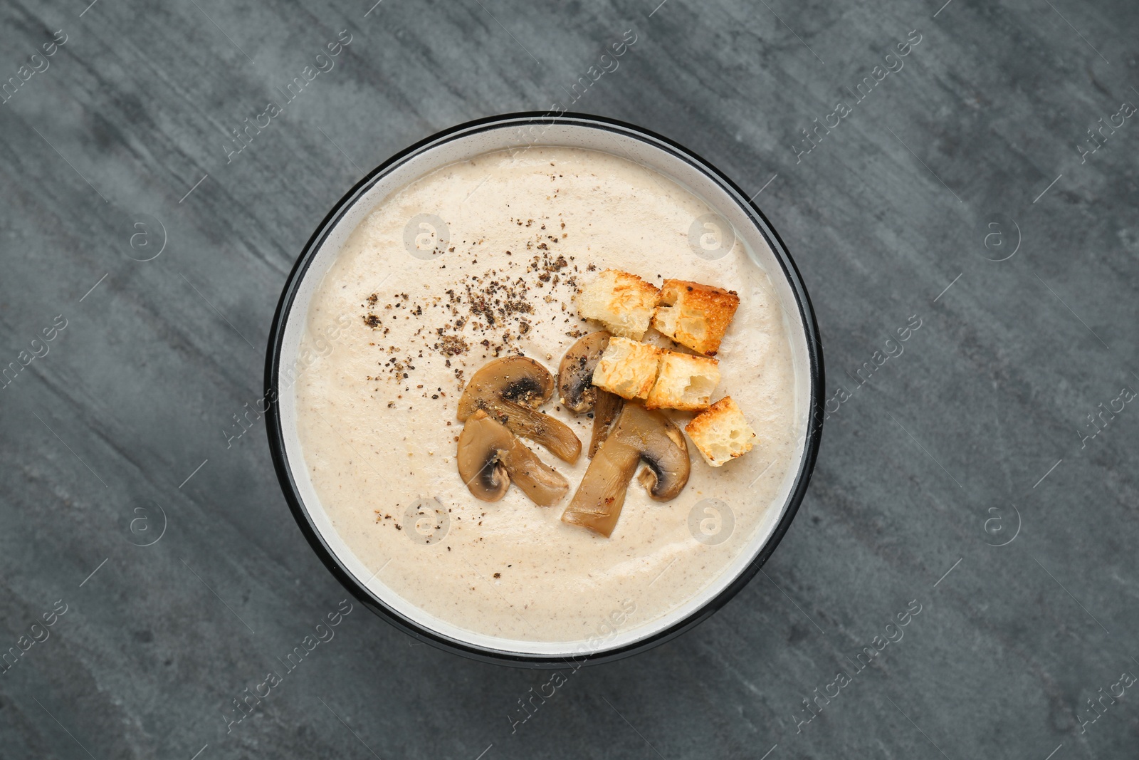 Photo of Delicious cream soup with mushrooms and croutons on black table, top view