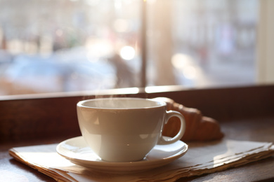 Photo of Delicious morning coffee, newspaper and croissant near window, indoors