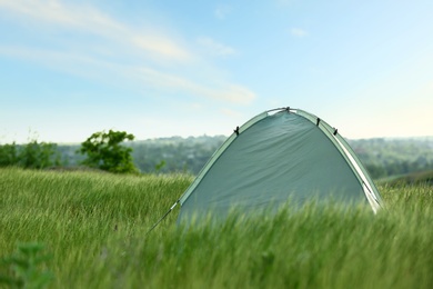 Photo of Modern camping tent in green field on sunny day. Space for text